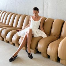 Female fashion influencer Rikke Krefting Ulstein poses on a vintage DS600 sofa with a slicked back bun wearing a sleeveless white corset mini dress and black Alaia mesh Mary Jane flats