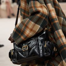 Chloe fall/winter 2024 show with a model wears the camera bag in black and a plaid jacket.