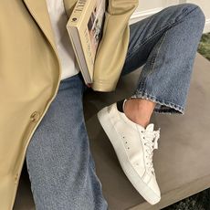 Woman wearing jeans, white sneakers, and a camel coat.