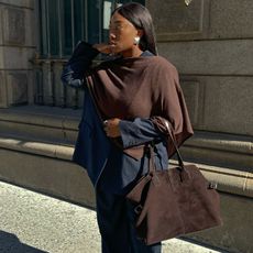 A woman wears a chocolate brown cape, blue pinstripe pants suit and a brown suede bag.