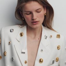 Woman wears white suit pinned with several Heaven Mayhem gold and silver earrings.