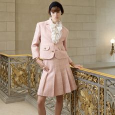 A woman wearing a black headband, pink blazer, ruffle blouse, and pink skirt for Celine's spring/summer 2025 collection.